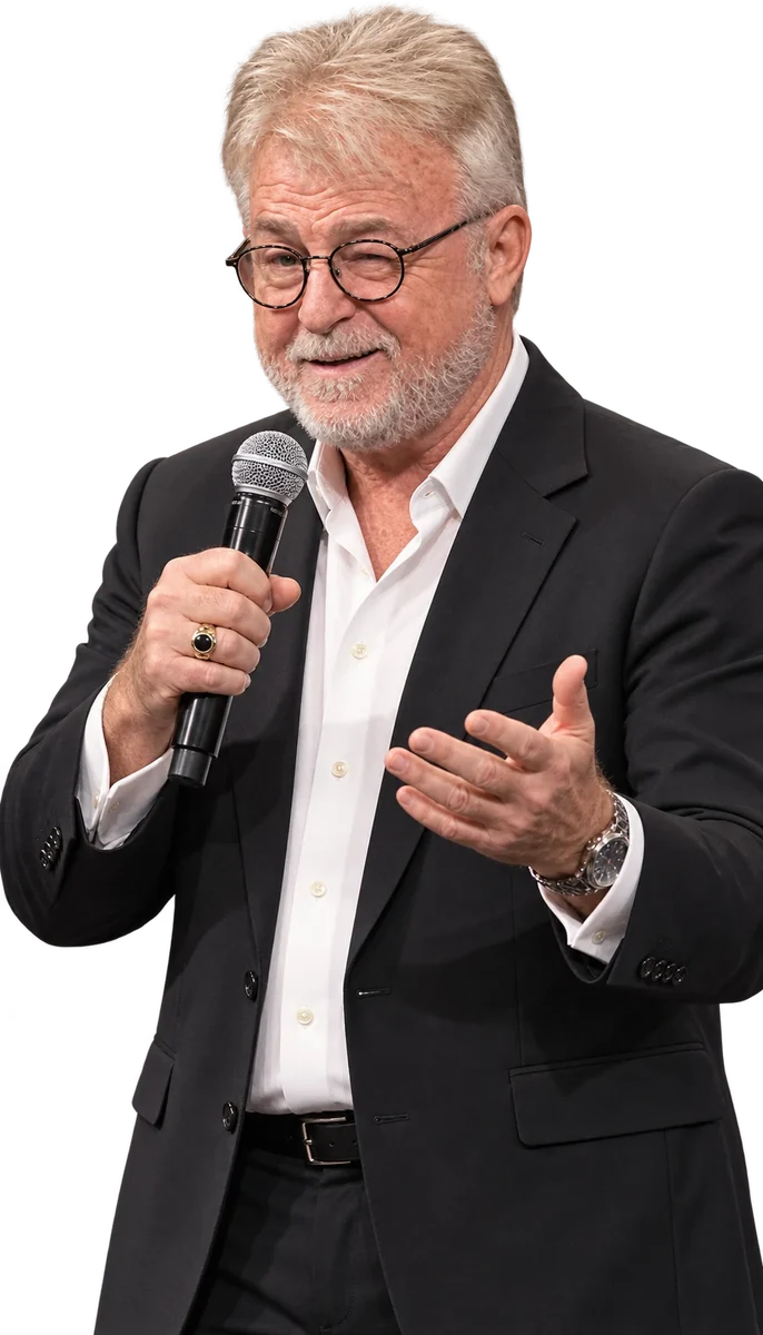Greg Langford in a black suit, speaking into a microphone