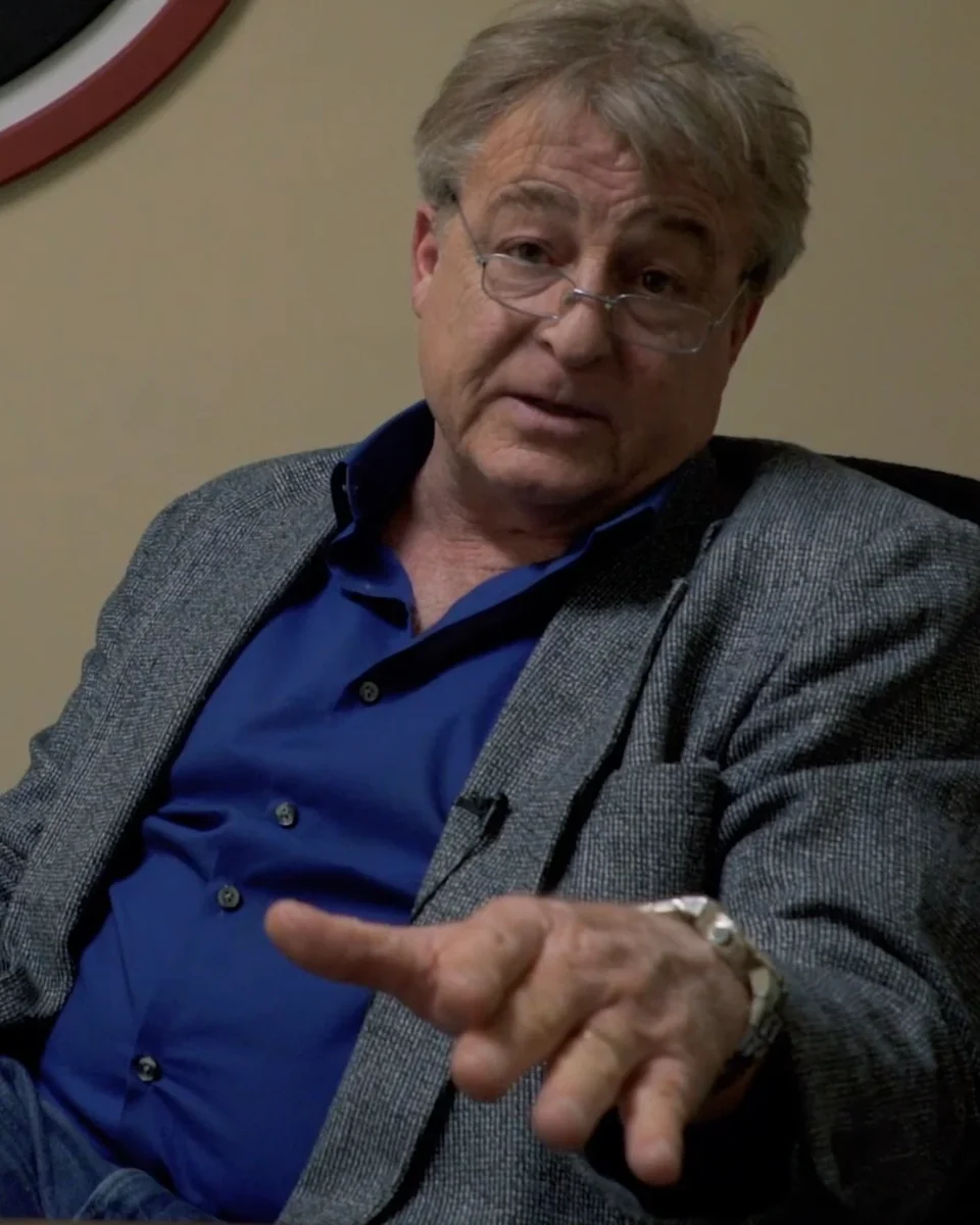 Greg Langford in a blazer, making a point during an interview