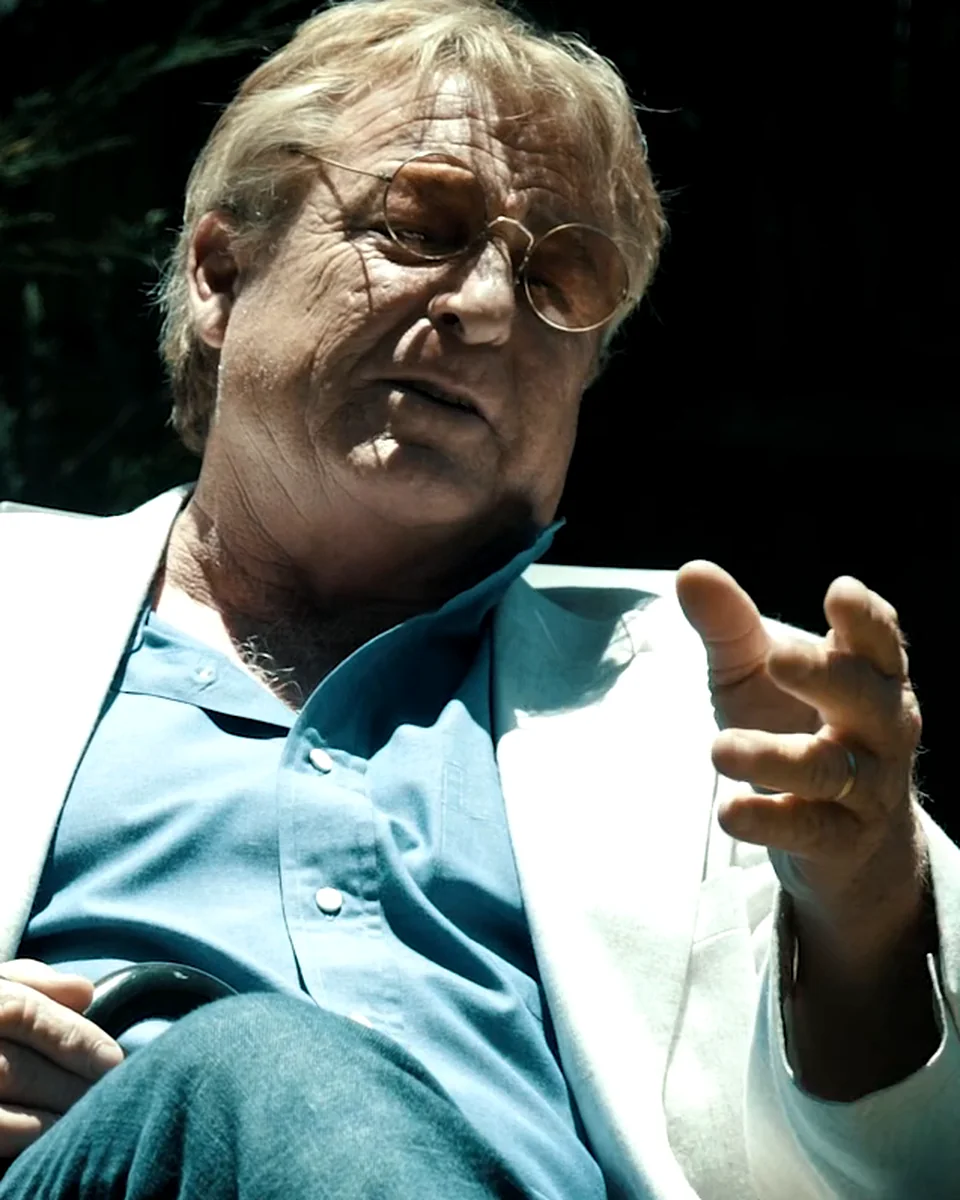 Greg Langford in a white blazer, cinematic still